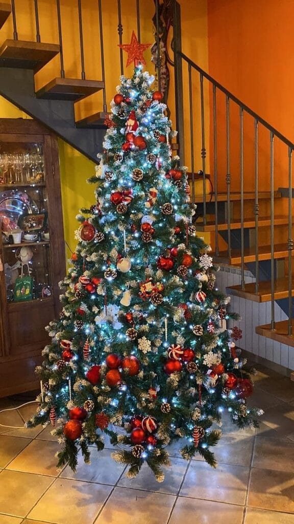 Albero di Natale decorato con pigne, luci e ornamenti rossi e dorati.